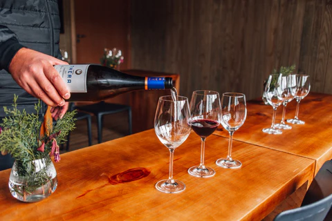 Algumas taças de vinho com uma pessoa segurando a garrafa de vinho e colocando na taça
